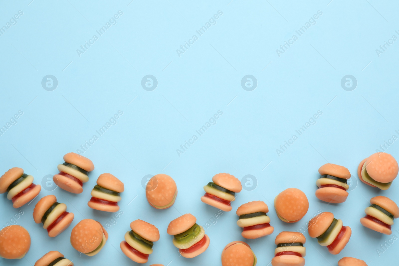 Photo of Tasty jelly candies in shape of burger on light blue background, flat lay. Space for text