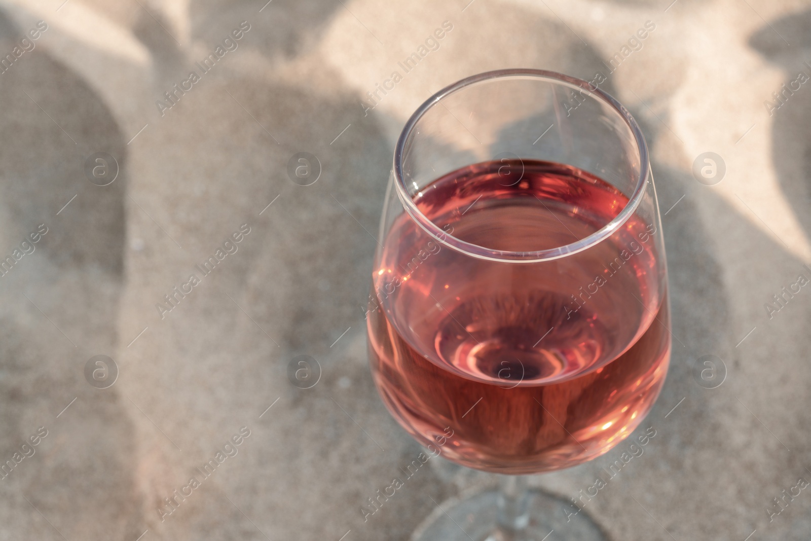 Photo of Glass of tasty rose wine on sand, closeup. Space for text