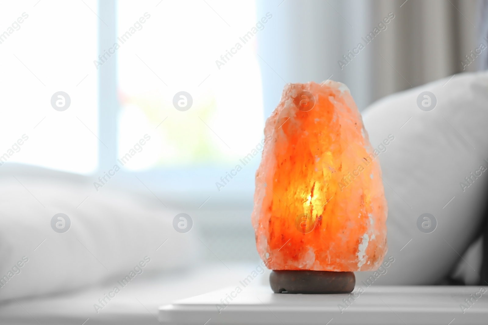 Photo of Himalayan salt lamp on table in bedroom. Space for text