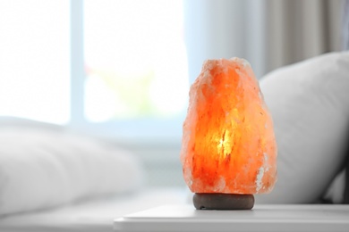 Photo of Himalayan salt lamp on table in bedroom. Space for text