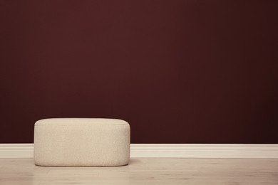 Stylish beige ottoman near brown wall indoors