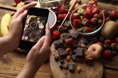 Blogger taking picture of chocolate and fruits at table, closeup