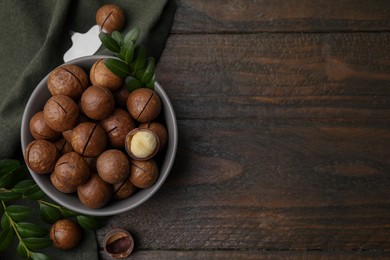 Photo of Tasty Macadamia nuts in bowl and green twigs on wooden table, flat lay. Space for text