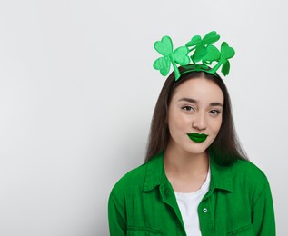 Image of St. Patrick's day party. Pretty woman with green lips and clover headband on light background. Space for text