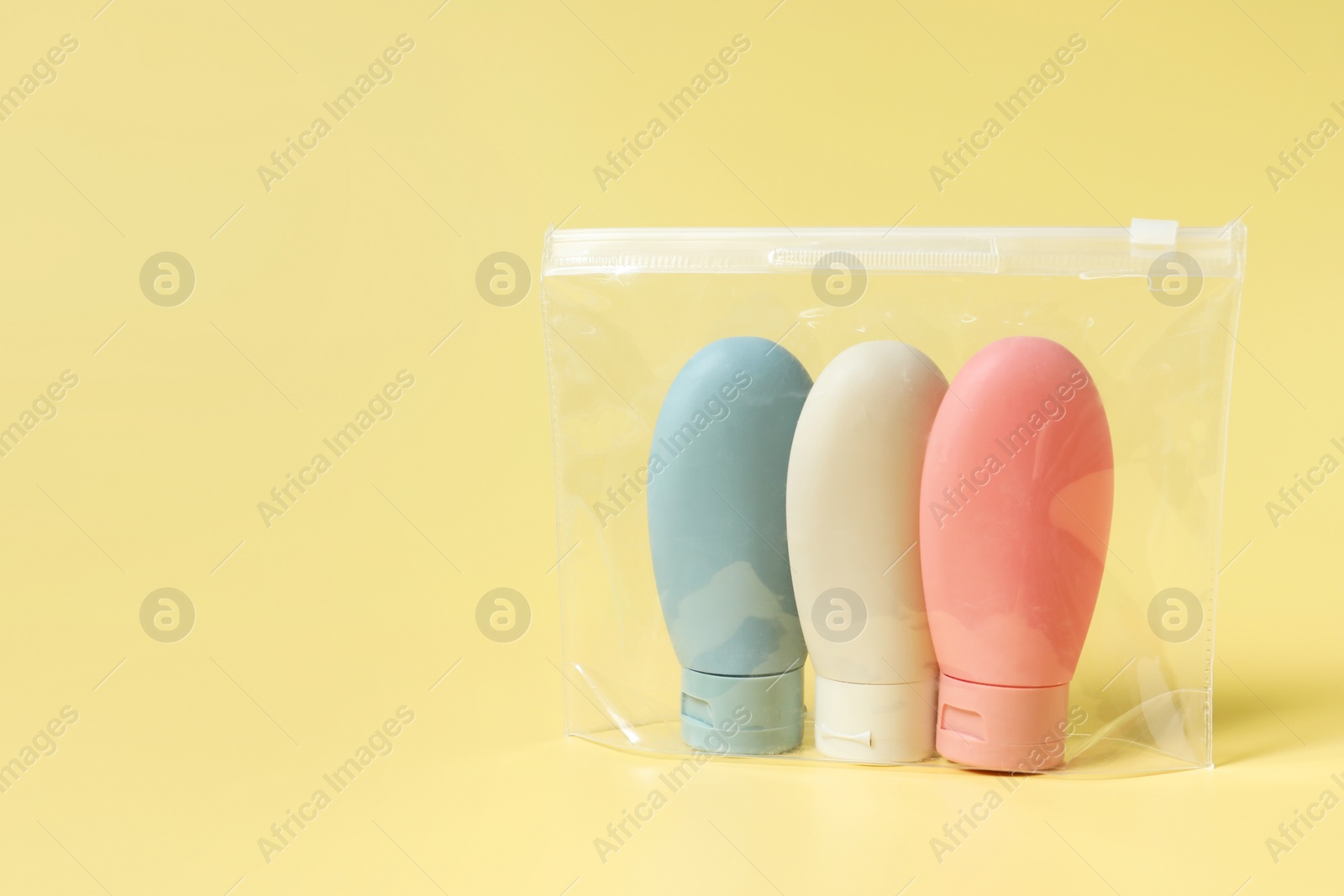 Photo of Cosmetic travel kit in plastic bag on yellow background, space for text