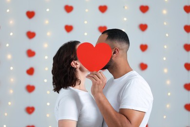 Lovely couple kissing behind red paper heart indoors. Valentine's day celebration
