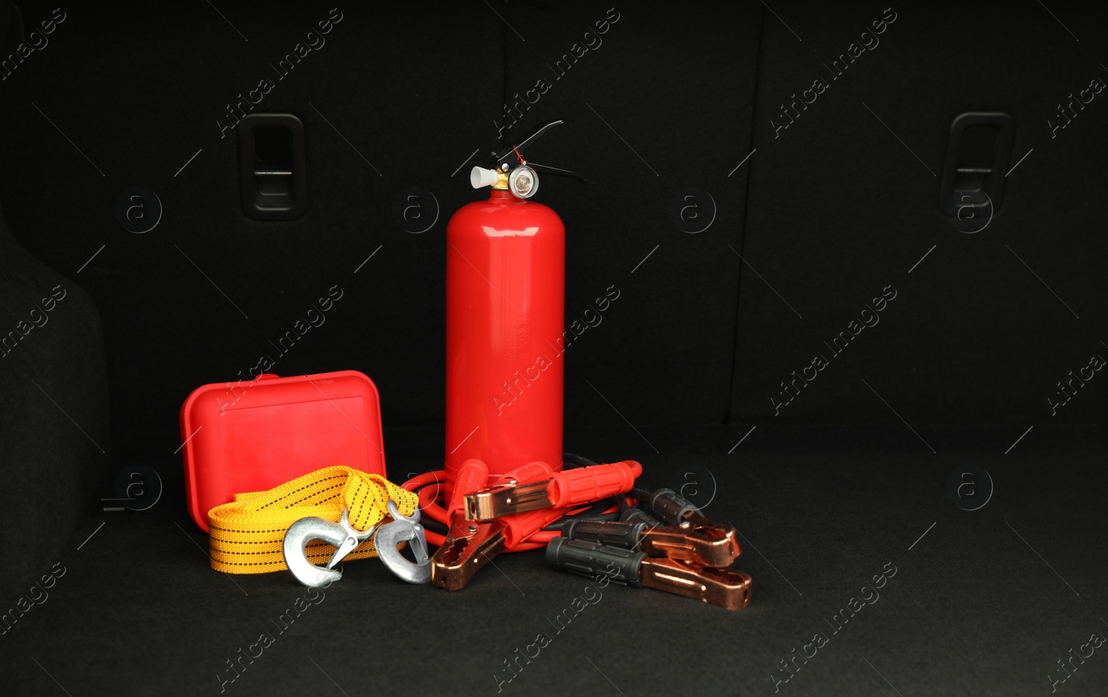 Photo of Red fire extinguisher, battery jumper cables, towing strap and first aid kit in trunk, space for text. Car safety