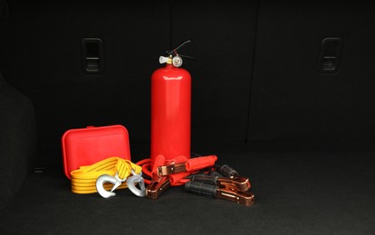 Photo of Red fire extinguisher, battery jumper cables, towing strap and first aid kit in trunk, space for text. Car safety