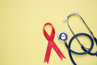 Photo of Red ribbon and stethoscope on yellow background, flat lay with space for text. AIDS disease awareness