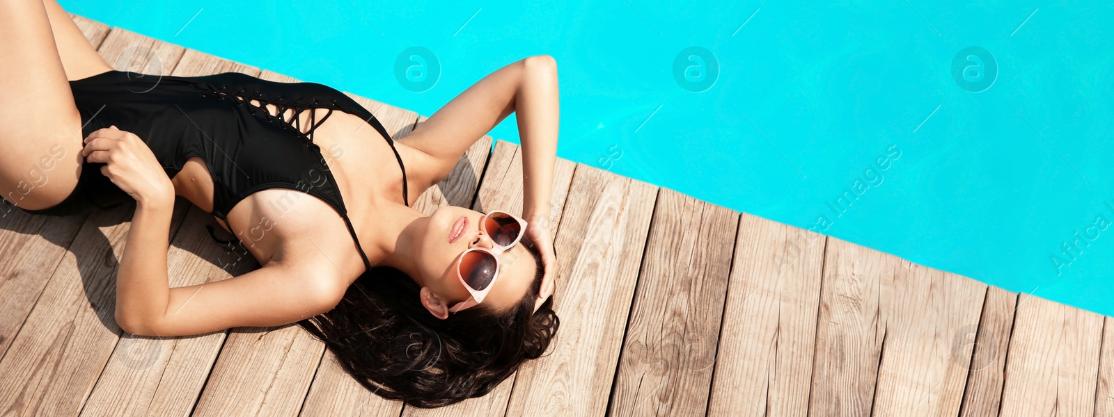 Image of Beautiful young woman lying near swimming pool on sunny day, banner design