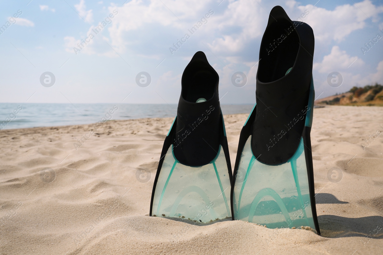 Photo of Pair of turquoise flippers on sandy beach near sea. Space for text