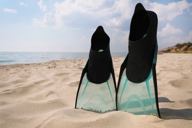 Photo of Pair of turquoise flippers on sandy beach near sea. Space for text
