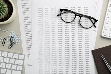 Photo of Accounting documents, glasses, computer keyboard and stationery on beige table, flat lay