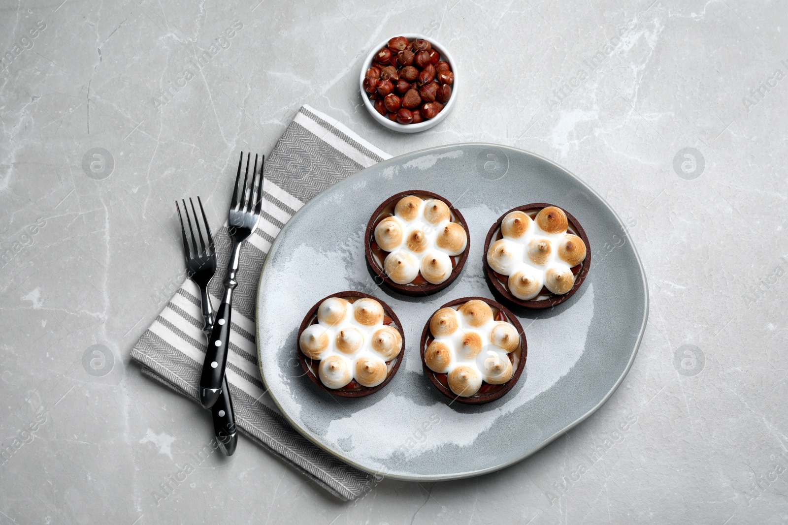 Photo of Delicious salted caramel chocolate tarts with meringue and hazelnuts on light grey table, flat lay