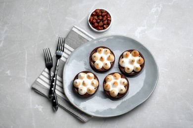 Photo of Delicious salted caramel chocolate tarts with meringue and hazelnuts on light grey table, flat lay