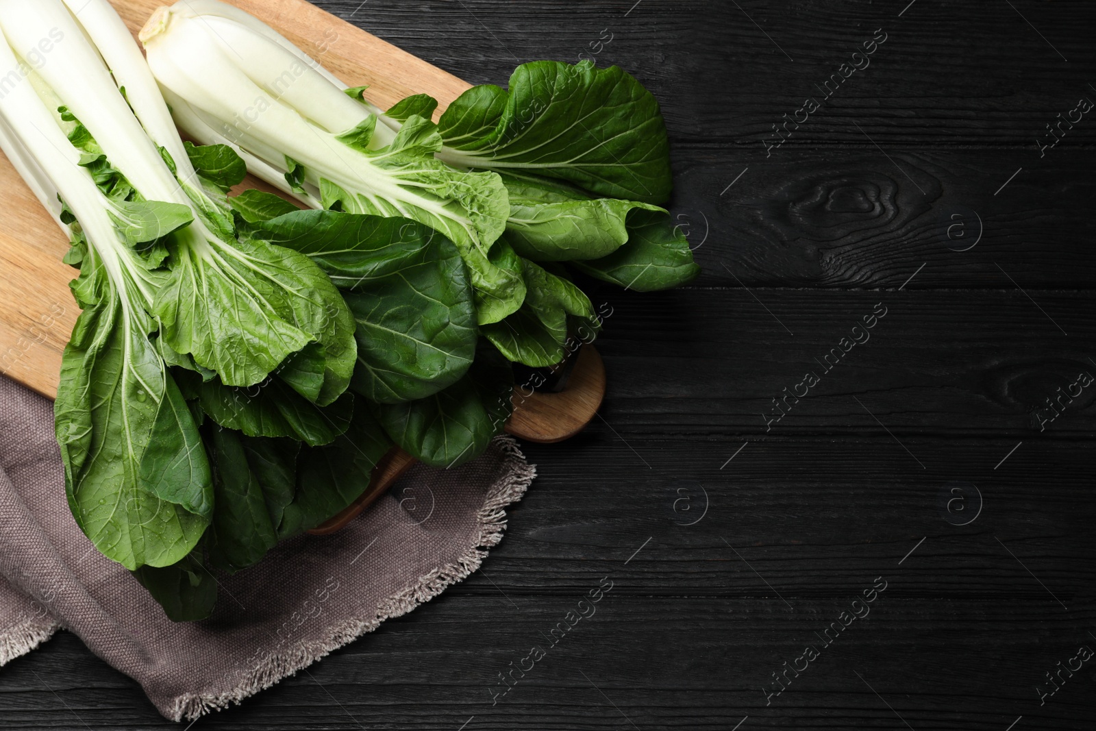 Photo of Fresh green pak choy cabbages on black wooden table, top view. Space for text