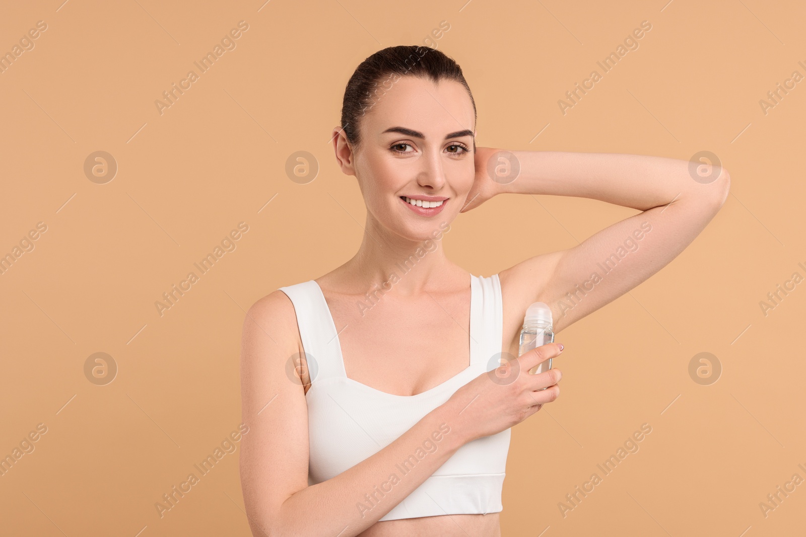 Photo of Beautiful woman applying deodorant on beige background