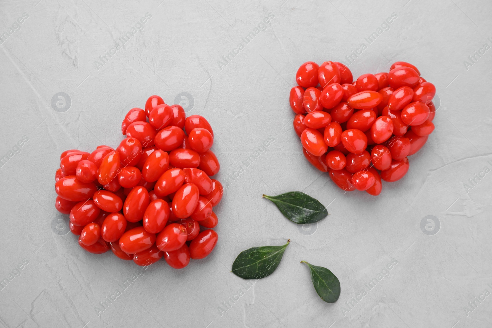 Photo of Hearts made of fresh goji berries and leaves on grey background, flat lay