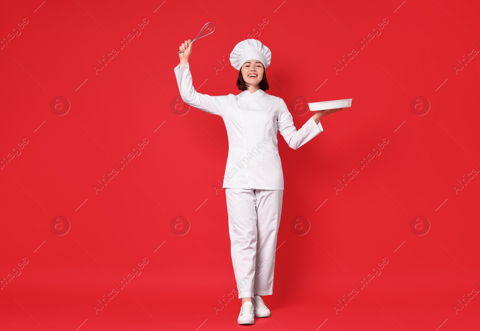 Photo of Happy confectioner holding whisk and baking dish on red background