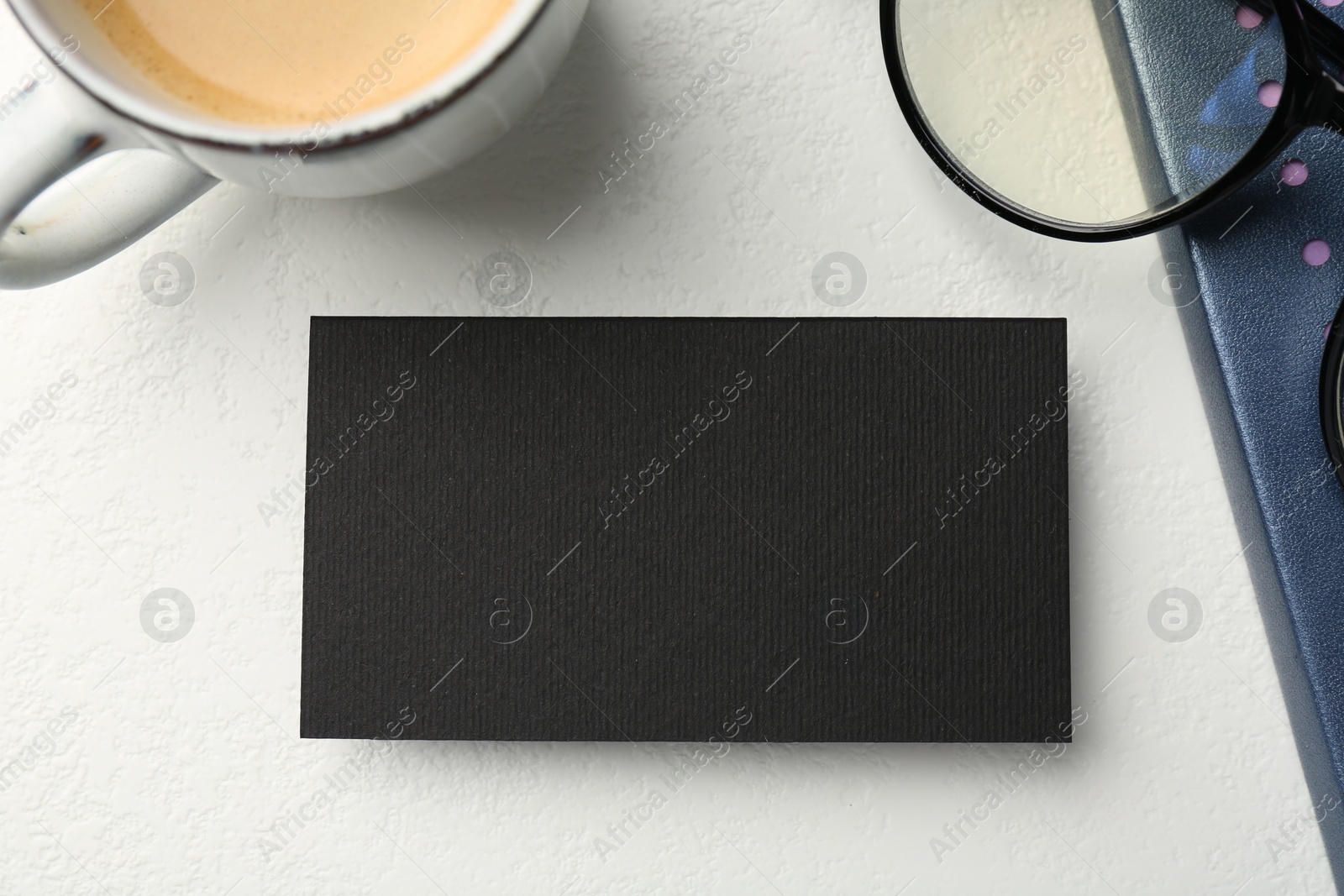Photo of Blank black business card, cup of coffee, glasses and stationery on white table, top view. Mockup for design