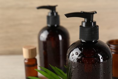 Shampoo bottles, essential oil and green leaf on white wooden table, closeup. Space for text