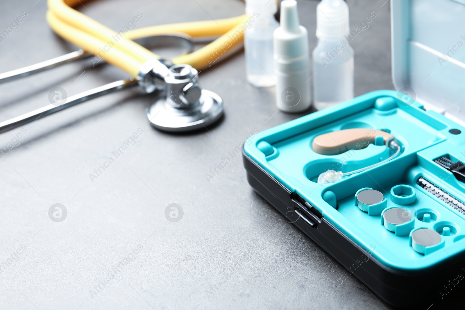 Photo of Hearing aid case and other medical objects on grey table. Space for text