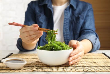 Photo of Woman eating Japanese seaweed salad at table, closeup