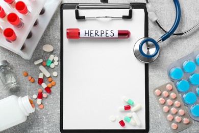 Photo of Test tube with word Herpes, different pills, clipboard and stethoscope on light grey table, flat lay. Space for text