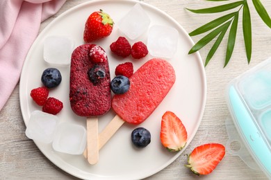 Photo of Plate of tasty berry ice pops on light wooden table, flat lay. Fruit popsicle