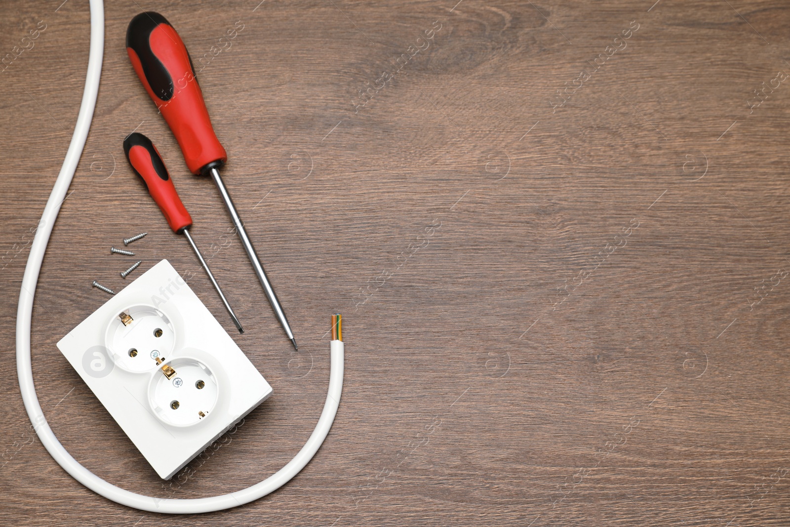 Photo of Power socket, screwdrivers and cable on wooden table, flat lay. Space for text