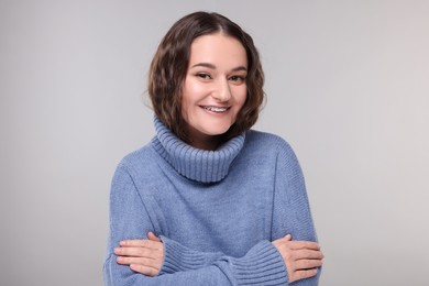 Smiling woman with dental braces in warm sweater on grey background