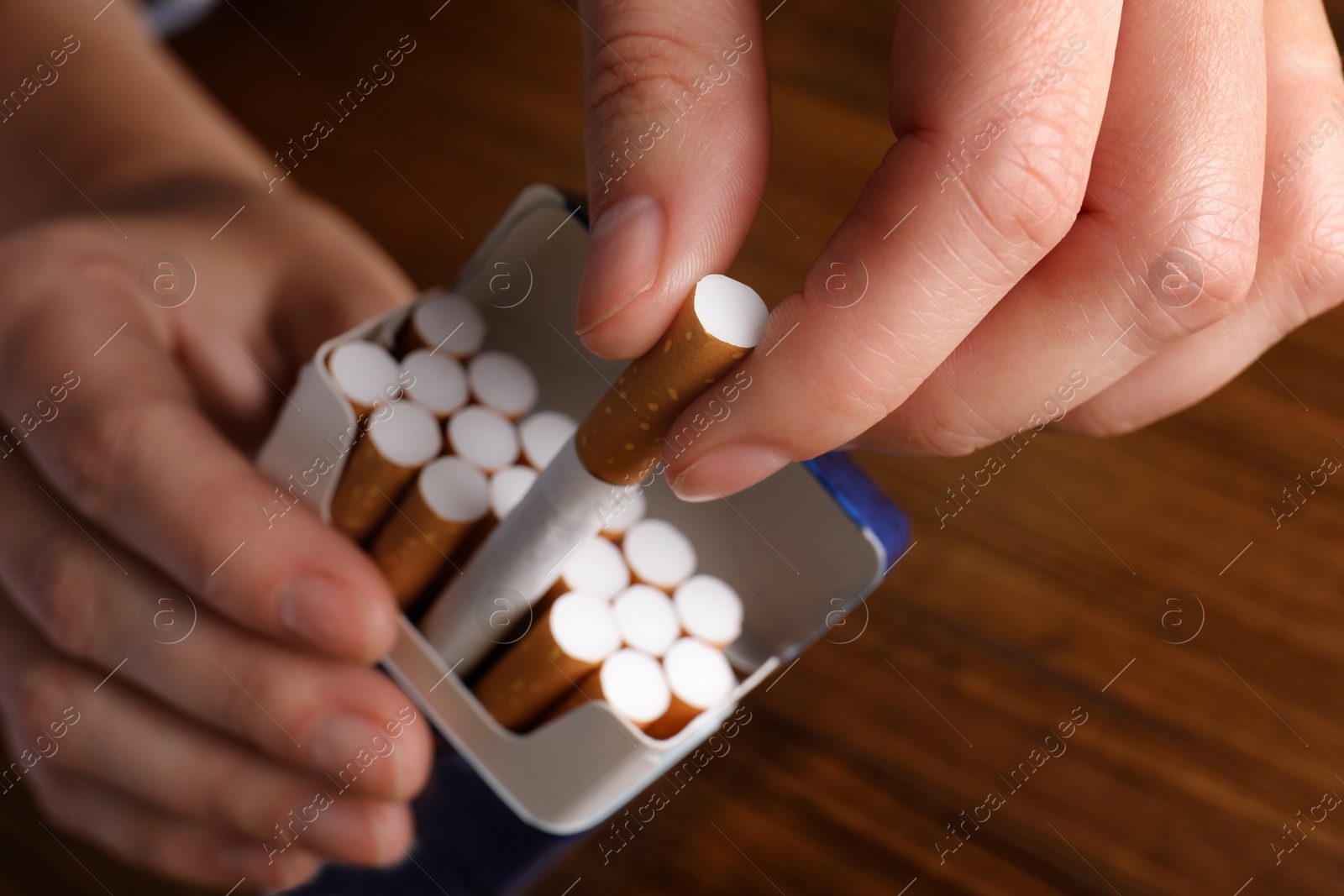 Photo of Woman taking cigarette out of pack at wooden table, closeup