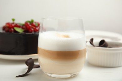 Photo of Glass of coffee, delicious cake and chocolate curls on white table