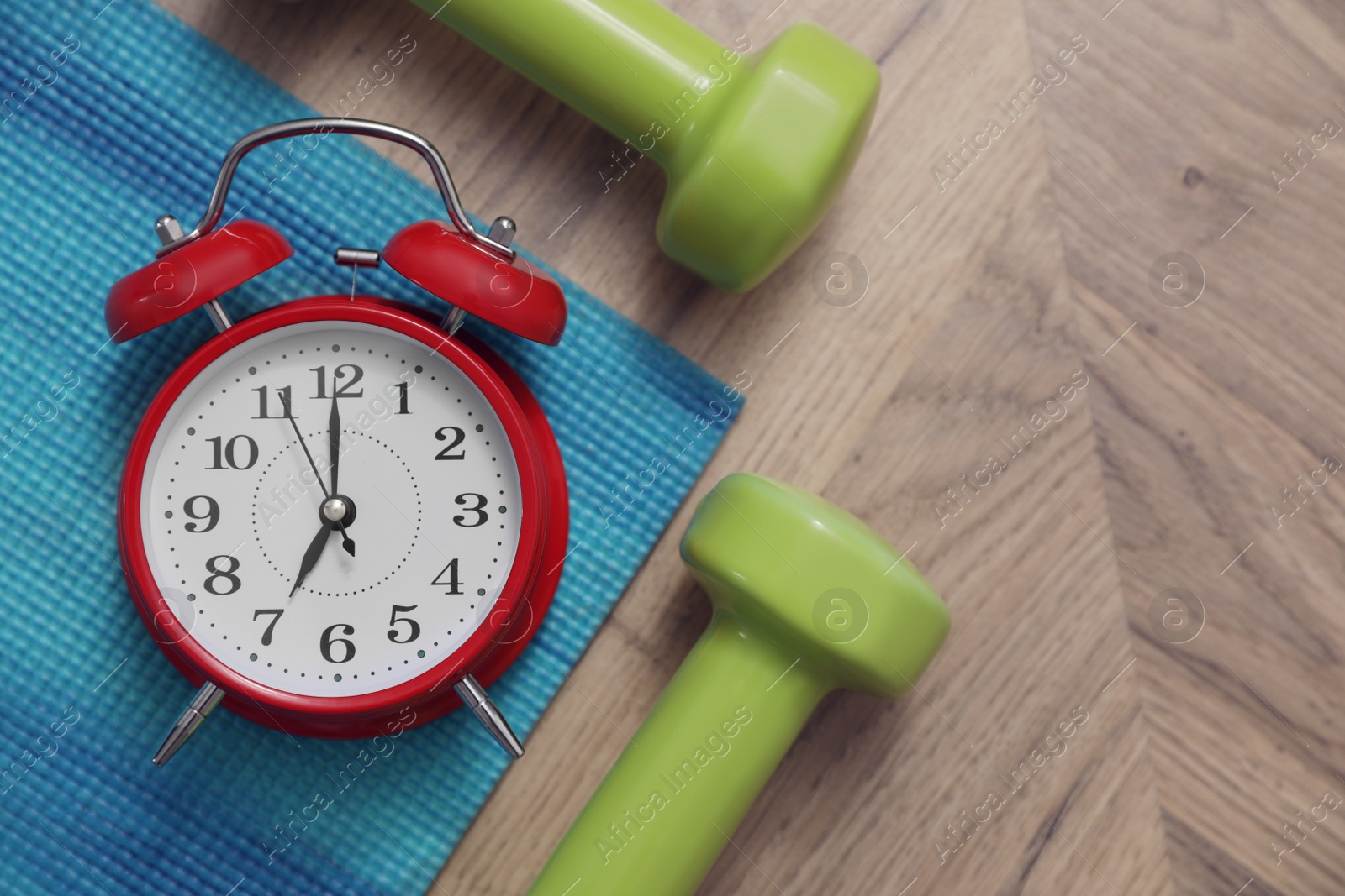 Photo of Alarm clock, yoga mat and dumbbells on wooden background, flat lay. Morning exercise