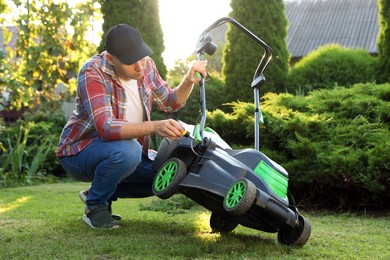 Photo of Man with screwdriver fixing lawn mower in garden on sunny day