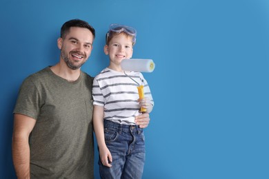 Photo of Father and son with roller near blue wall, space for text. Repair work