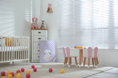 Photo of Crib, table and chairs with bunny ears in stylish baby room interior