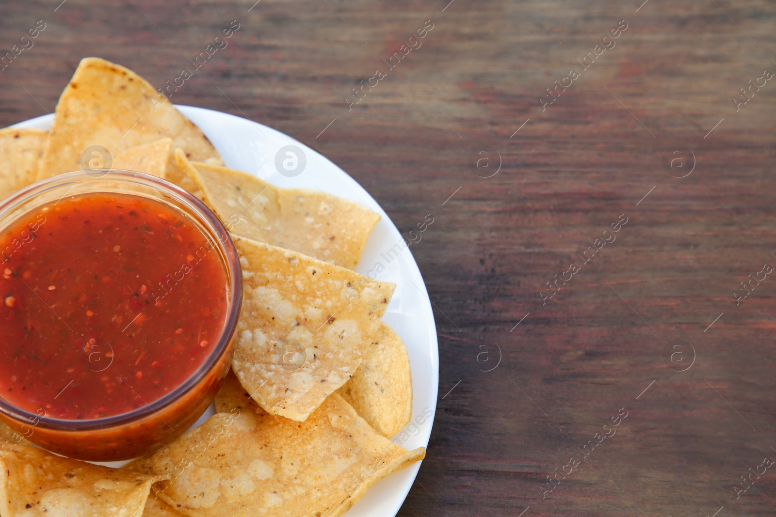 Photo of Tasty salsa sauce and tortilla chips on wooden table, closeup. Space for text