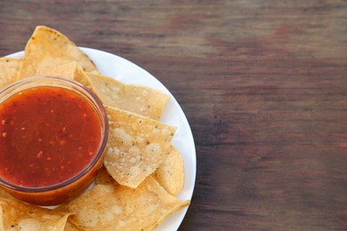 Tasty salsa sauce and tortilla chips on wooden table, closeup. Space for text