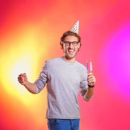 Portrait of happy man with party cap and champagne in glass on color background