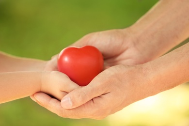 Photo of Adult and child hands holding heart on blurred background, closeup. Family concept