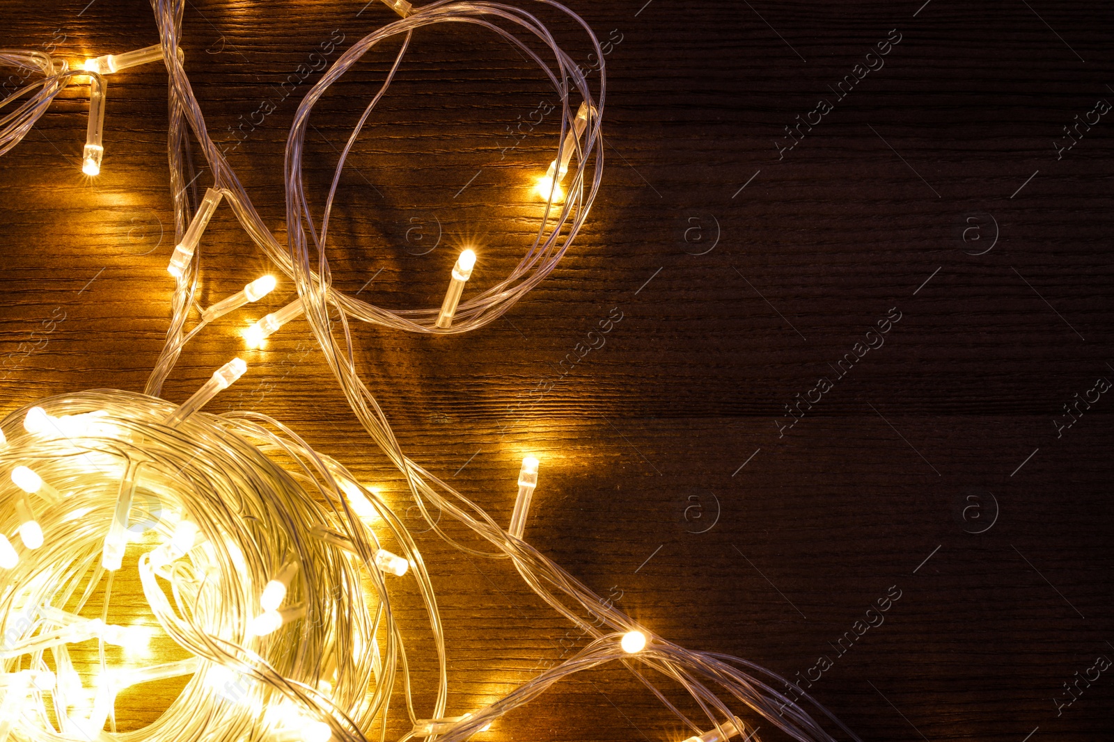 Photo of Beautiful glowing Christmas lights on wooden table, top view. Space for text