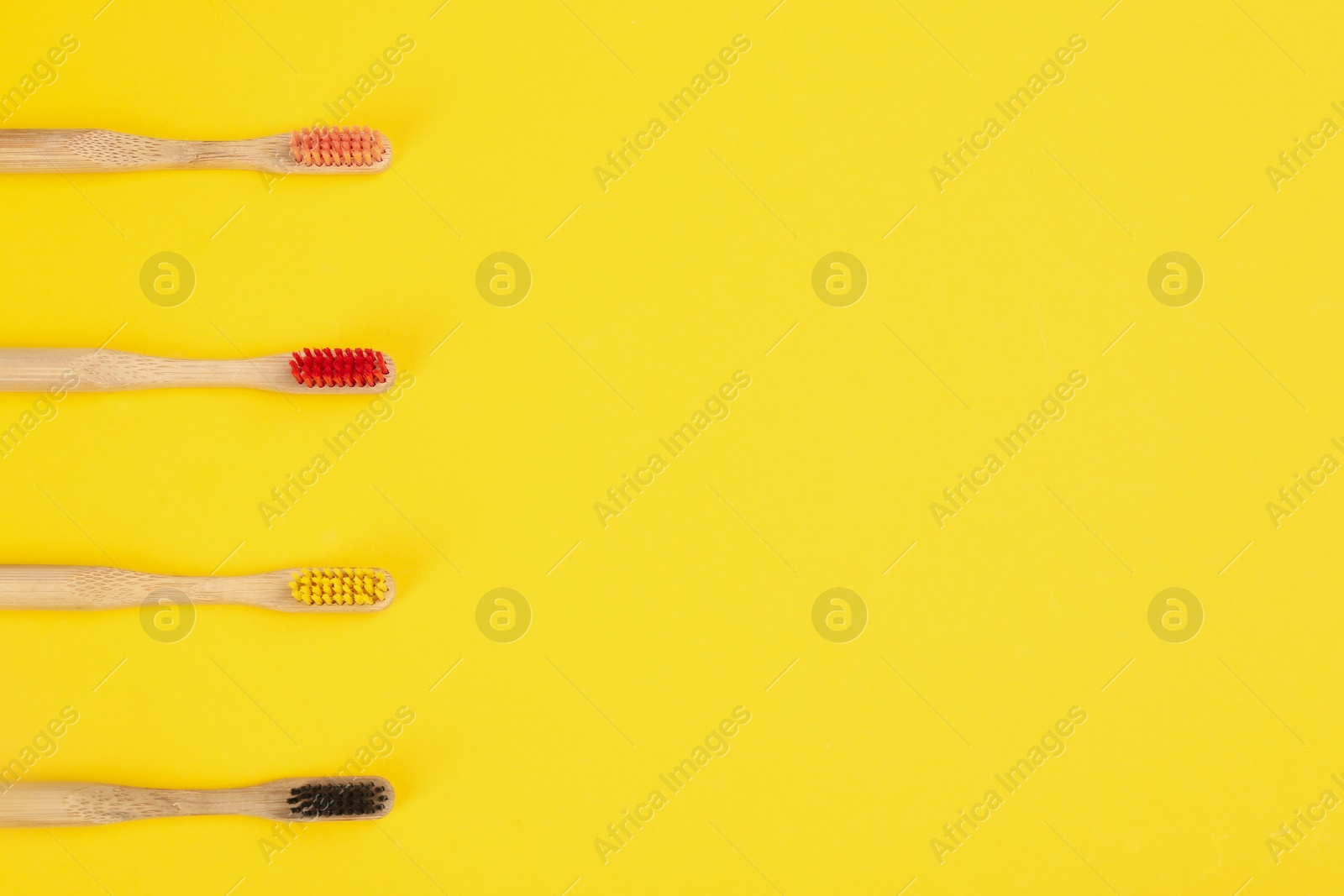 Photo of Toothbrushes made of bamboo on yellow background, flat lay. Space for text