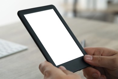 Photo of Man using e-book reader at wooden table indoors, closeup