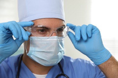 Doctor in protective mask, glasses and medical gloves against light background