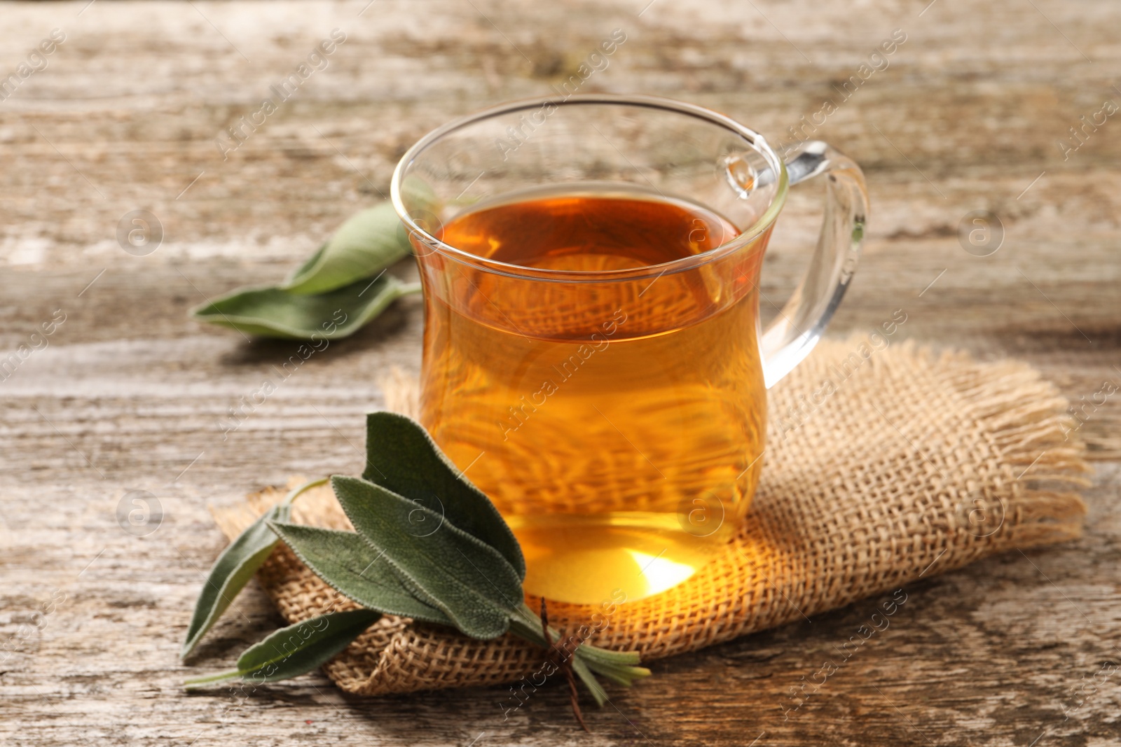 Photo of Cup of aromatic sage tea and fresh leaves on wooden table