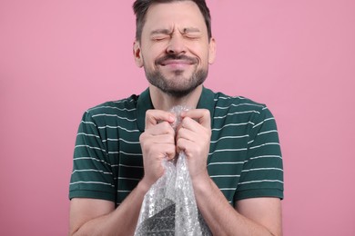 Man popping bubble wrap on pink background, closeup. Stress relief