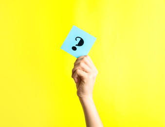Woman holding note with question mark on yellow background, closeup. Space for text