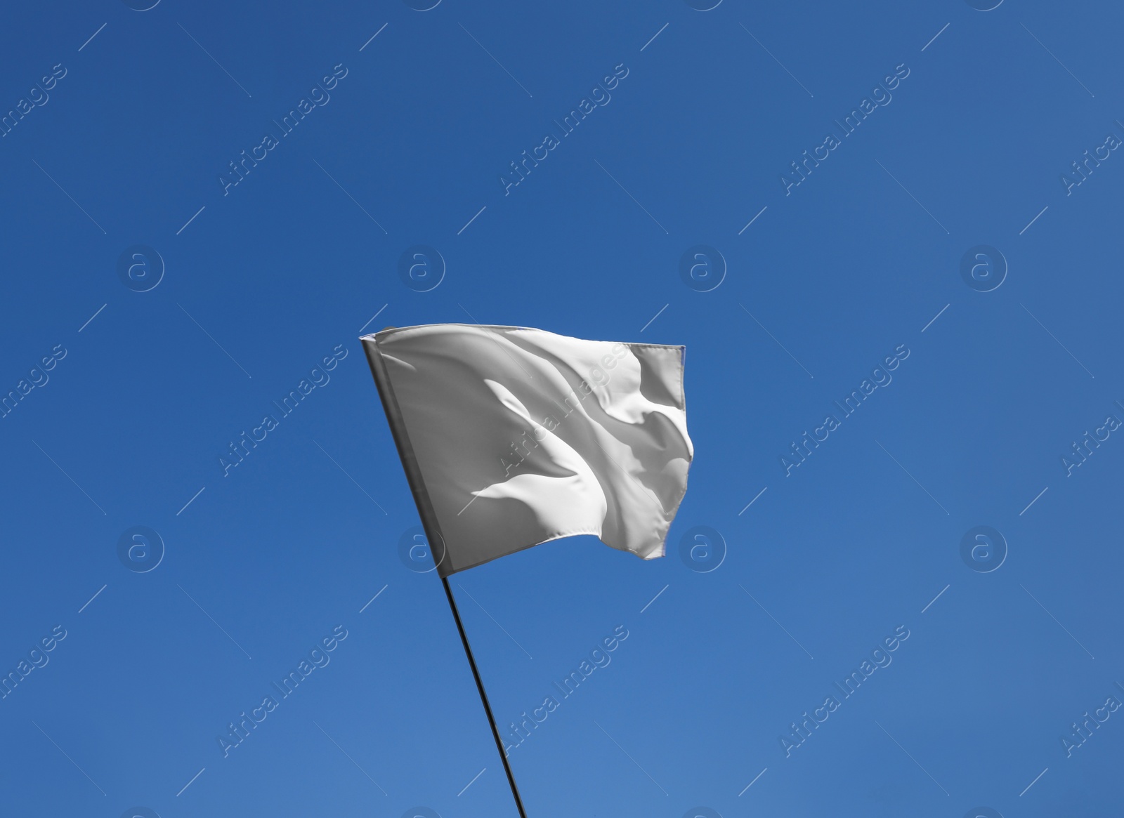 Photo of White flag fluttering against blue sky on sunny day