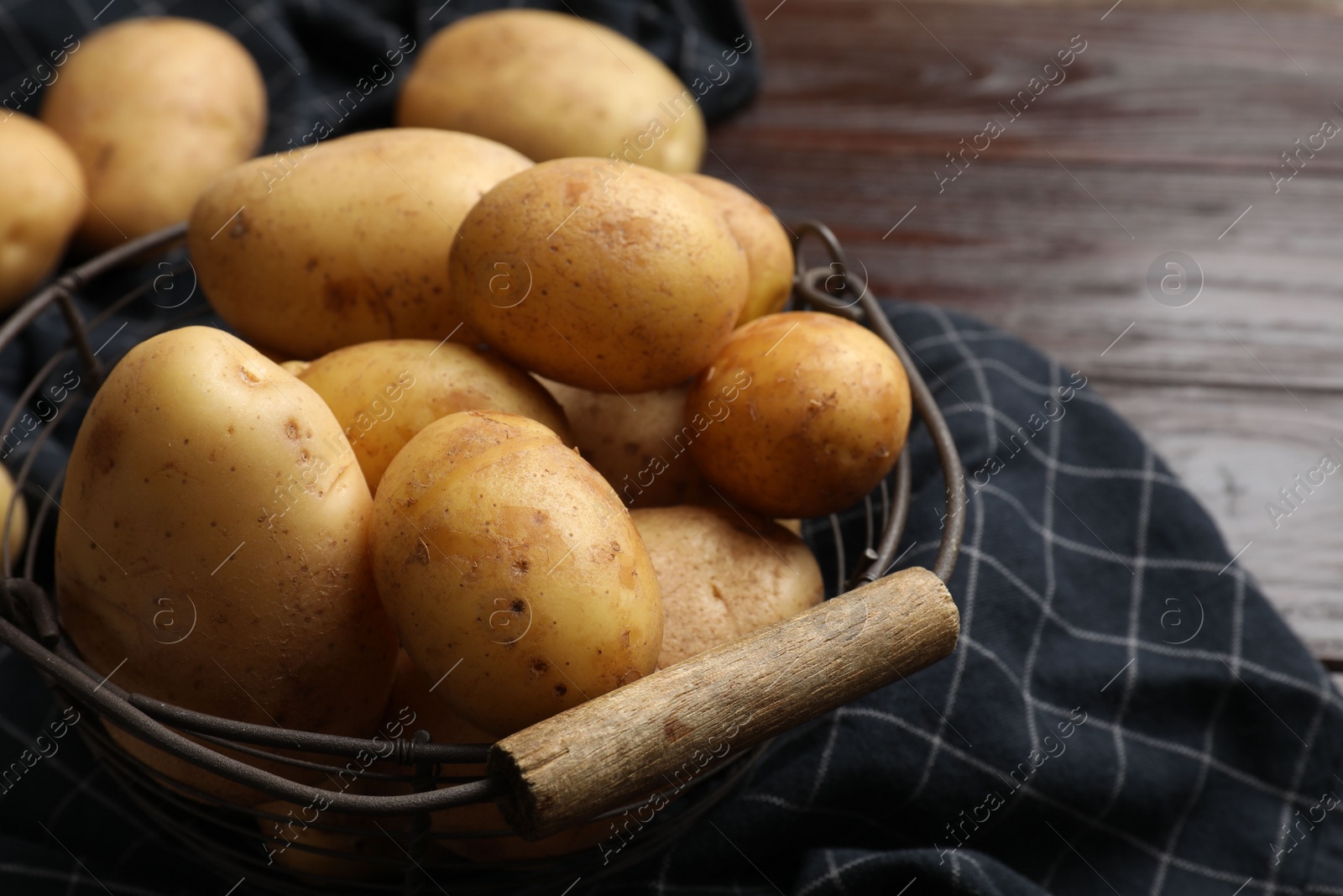 Photo of Raw fresh potatoes in metal basket on wooden table, closeup